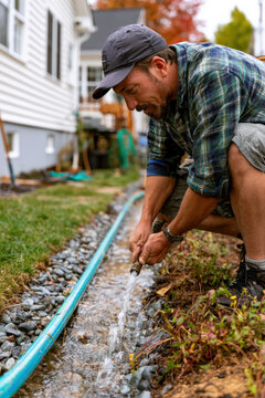 Man waters garden bed with blue hose