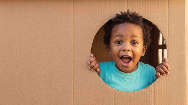 Toddler boy looking through a hole in a cardboard box playing and smiling with excitement
