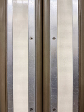 Close-up of a subway train door featuring symmetrical metal panels, screws, textured strips and visible surface scratches from everyday use, highlighting details of urban public transportation design.