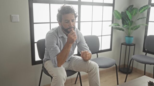 Man sitting with hands on face and bowed head in clinic waiting room; anxiety thinking pondering reflection.