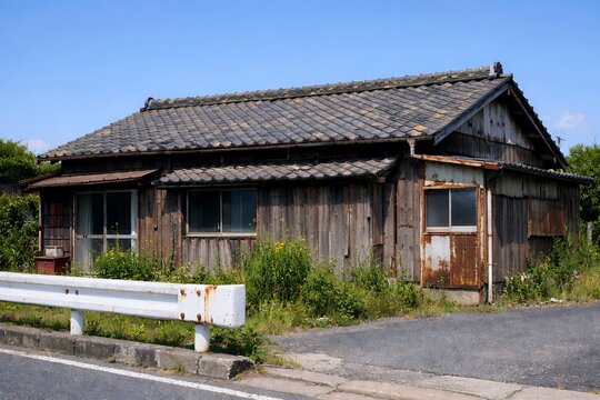 夏の青空の下にひっそり佇む朽ちた日本家屋と道