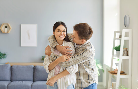 Married couple spending time together. Two young people in love embracing each other. Happy, smiling man and woman hugging standing in the living room at home