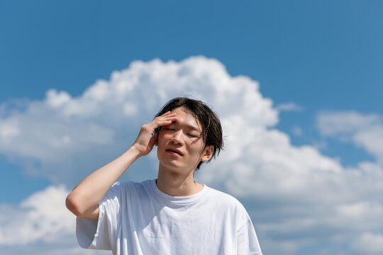 青空の下で暑さに耐える若い男性夏バテ頭痛めまい体調不良の症状