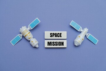 Miniature satellites with wooden blocks text "SPACE MISSION" on a purple background. Representing aerospace exploration and technology concepts © MY STOCKERS