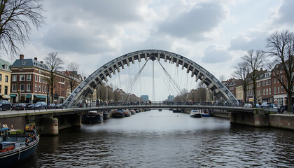 Naklejka premium Arched steel bridge with cables spanning canal waterway surrounded by multi-story brick buildings with gabled roofs and moored boats along edges