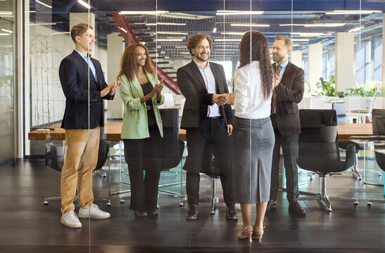 Business people handshake partners agreement success meeting. In a modern boardroom colleagues applaud the team as partners sign a contract and mark progress. Concept shows trust and partnership.