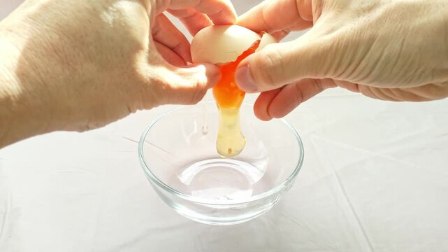 キッチンで透明なガラスボウルに新鮮な生卵を割る手元の動作