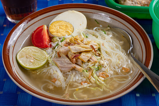 Clear broth chicken soto soup with rice egg lime tomato served in a traditional indonesian warung setting