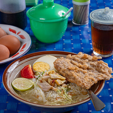 Indonesian chicken soto soup with boiled egg and crispy fritter served in traditional blue checkered warung setting