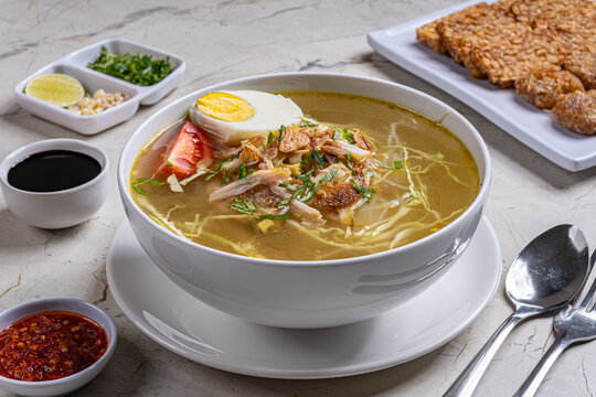 Traditional indonesian chicken soto soup with boiled egg sambal and fried tempeh in bright modern marble setting