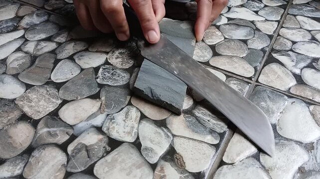 A Man Sharpening Large Kitchen Knife on Whetstone Outdoors