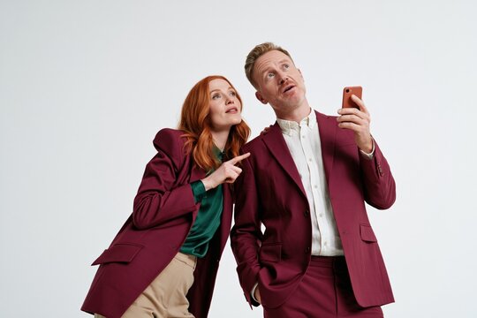 Two colleagues in coordinated burgundy suits looking up at a smartphone for teamwork and corporate presentation banner or editorial use
