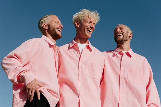 Three friends in matching pink shirts laughing together under a blue sky for lifestyle portrait and promotional banner use
