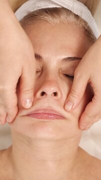 Closeup of a beautician's hands performing a professional anti aging face massage on a mature woman, focusing on lifting and sculpting the cheekbones for skin rejuvenation and relaxation