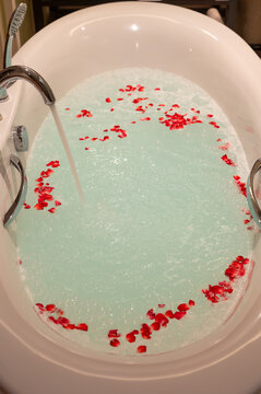 Bathtub filling with water and red rose petals.