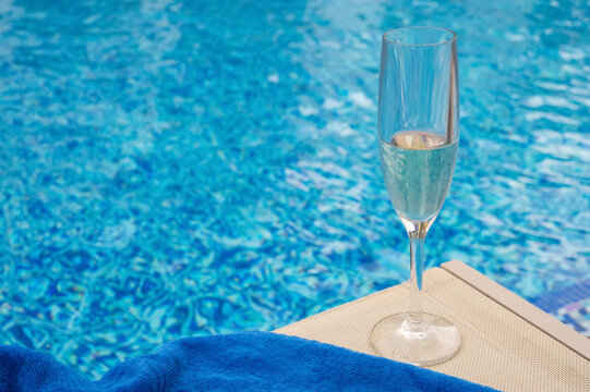 A glass of champagne and a blue towel on a pool lounger.