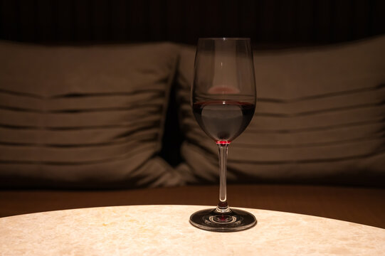 Glass of red wine on a marble table with soft cushions behind.