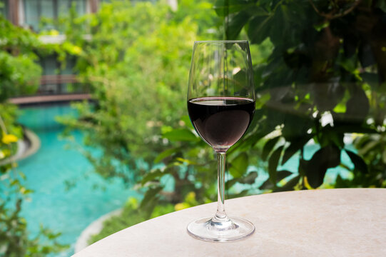 Glass of red wine on a table with a lush garden and swimming pool view.