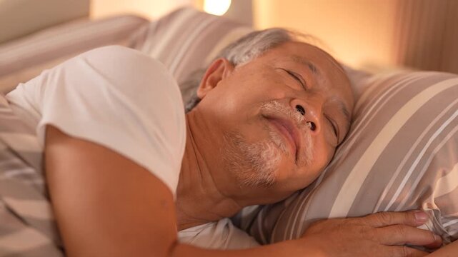Slow-motion close-up of an elderly man sleeping soundly on his side with a faint smile on his lips. Ultra HD geriatric nursing footage for health and insurance campaigns.