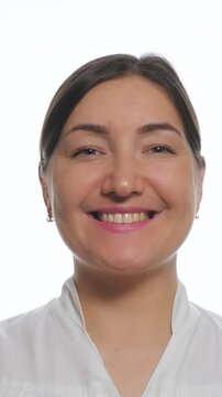 Close up of a happy woman looking at the camera and smiling. Gradually showing a beautiful. Broad smile. This charming brunette female doctor is isolated against a clean white background in a studio