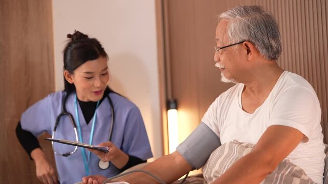 Nurse wraps a blood pressure cuff around the upper arm of a seated elderly man, then writes the reading onto her clipboard. Ultra HD geriatric nursing footage for health and insurance