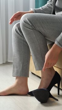Unrecognizable woman returning home, taking off her uncomfortable black high heeled shoes and massaging her aching feet, feeling relief from pain and fatigue after a hard day