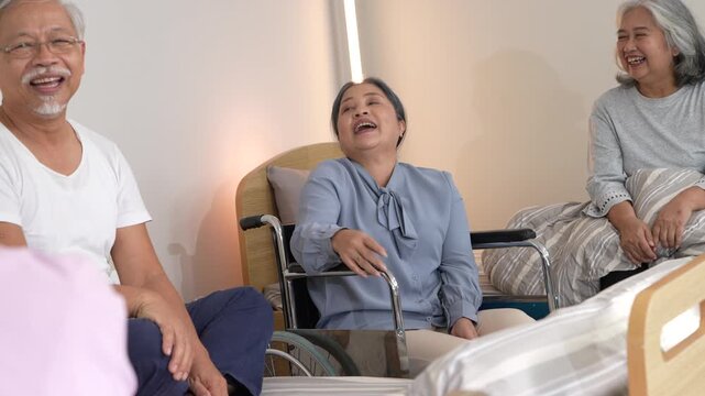 Three older adults talk and laugh across the beds, one in a wheelchair listening with her hands folded in her lap. Ultra HD senior wellbeing footage from a contemporary care ward.