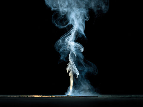 Smoke flame black background wispy upward blue match burn vapor from extinguished match rising in thin curl over dark surface, low light studio scene