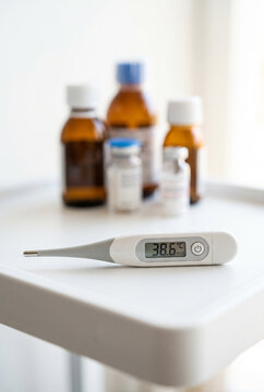 Digital thermometer on clean medical surface, medicine bottles softly blurred on background, healthcare and fever monitoring concept. Close-up.