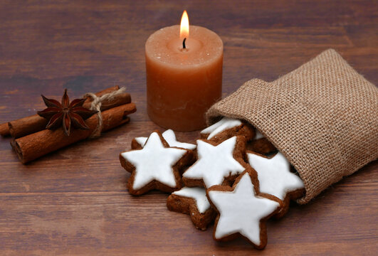 Cinnamon stars in a burlap bag with a lit candle, cinnamon sticks, and star anise on a wooden background.