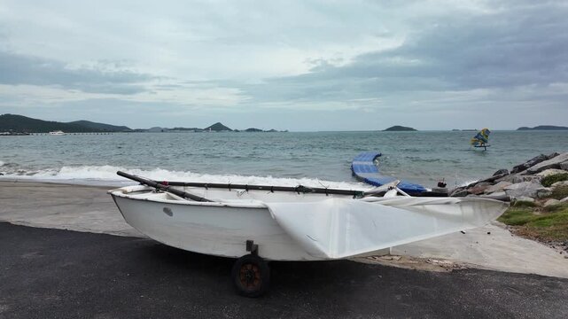 Small white dinghy boat on beach with sailboat sailing far away in sea on cloudy day