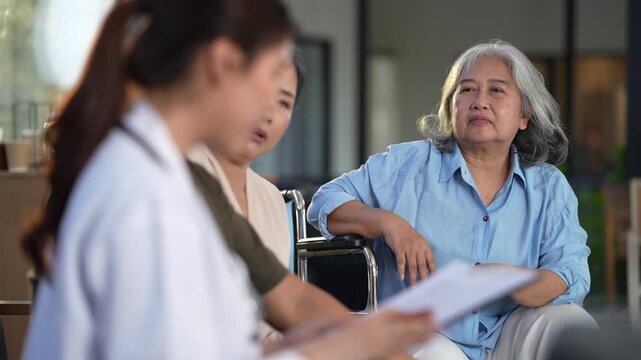 Doctor with a clipboard leans in to speak one to one with an elderly woman seated in a wheelchair. Ultra HD senior wellbeing footage from a contemporary care ward.