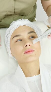 Young beautiful woman enjoying a rejuvenating facial treatment in a professional spa salon, where a beautician applies a cosmetic mask with a brush for deep cleansing and skin renewal