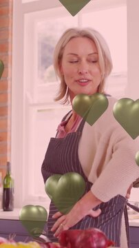 Animation of green hearts over couple in love cooking in kitchen