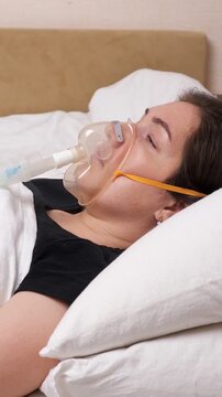 Sick woman with closed eyes resting in bed and wearing an oxygen mask for breathing support, illustrating home care for severe respiratory illness, asthma, or lung disease treatment