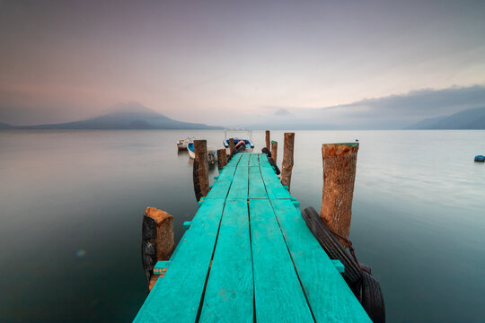 Turquoise pier and boats on misty mountain lake