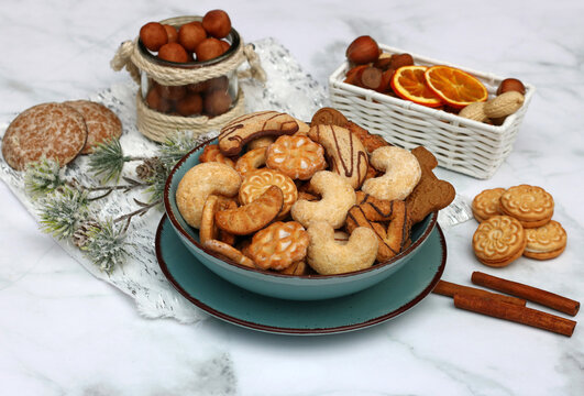 A large Christmas plate with an assortment of cookies, such as vanilla crescents, gingerbread, cinnamon sticks, and marzipan potatoes, set against a light marble background.
