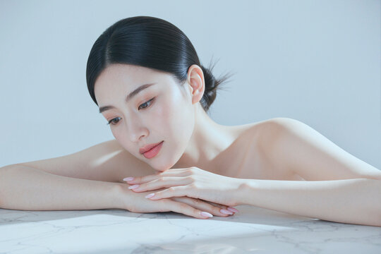 Close up of Asian young adult woman resting chin on folded hands, presenting skincare and beauty wellness concept. Ideal for spa, cosmetic treatment, self care branding