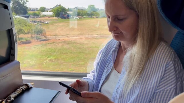 Woman types email reply on smartphone then gazes thoughtfully out train window during journey in slow motion. Concept of digital communication and quiet contemplation during business travel in 4K.