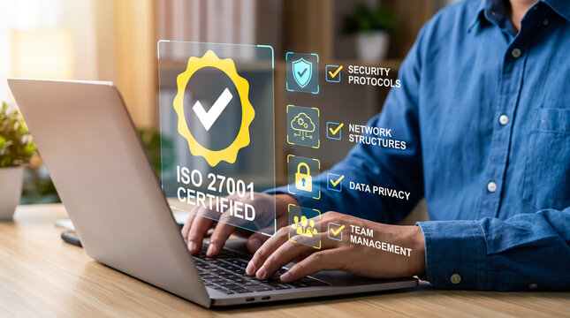 Businessman using laptop with iso 27001 certification hologram, security protocols, network structures, data privacy, and team management icons for cybersecurity compliance