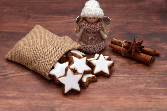Cinnamon stars in a burlap bag with a knitted angel figurine, cinnamon sticks, and star anise against a dark wooden background.