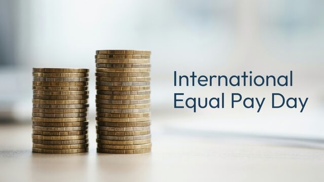 Two uneven stacks of gold coins sit on a wooden table. This represents the economic concept of wage inequality for International Equal Pay Day.