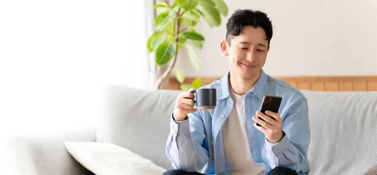 コーヒーを飲みながらスマートフォンを使う男性
