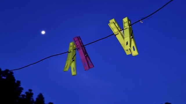 Colorful plastic clothespins clipped to a wire under a night sky clothespin peg clothesline line