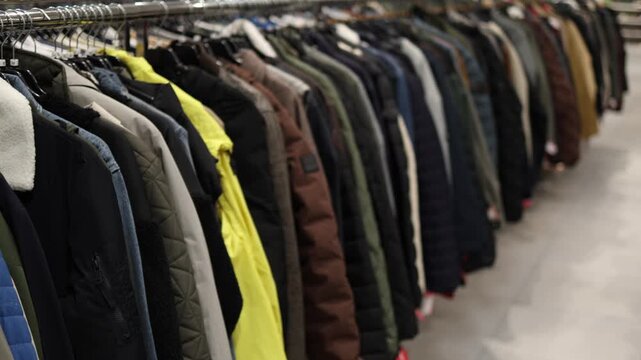 A close view of jackets and outerwear hanging on metal racks in a clothing store showing varied colors styles and seasonal apparel arranged for customers in retail stores