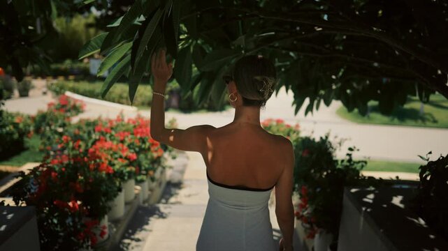 Female person enjoying nature in tropical garden, breathing fresh air, back view . Feel happiness, joy and unity with nature, sensual woman strolling alone in fabulous garden in luxury hotel, rearview