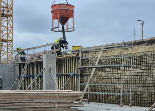 Construction workers pouring concrete into a wall formwork using a crane concrete skip funnel.
