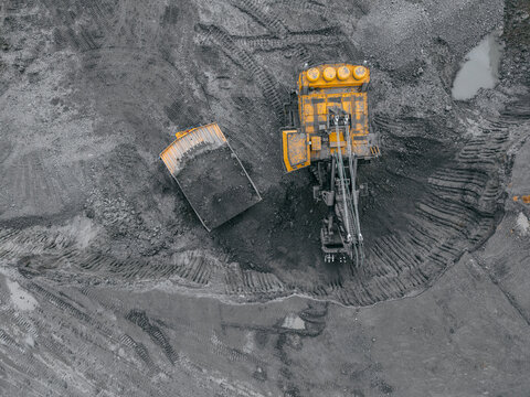 Aerial top view Excavator loading overburden soil into large quarry truck. Industrial coal deposit development, machinery at open pit mine extracting resources.