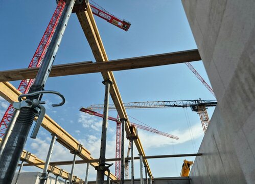 Adjustable steel props and wooden beams supporting concrete formwork with tower cranes in the background.