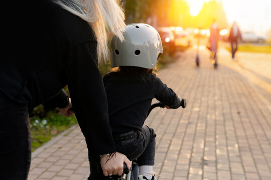 Father guides young daughter learning to ride bicycle on sunny pathway
